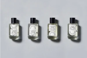 Four clear glass perfume bottles with black caps arranged in a row on a pale grey seamless studio backdrop.