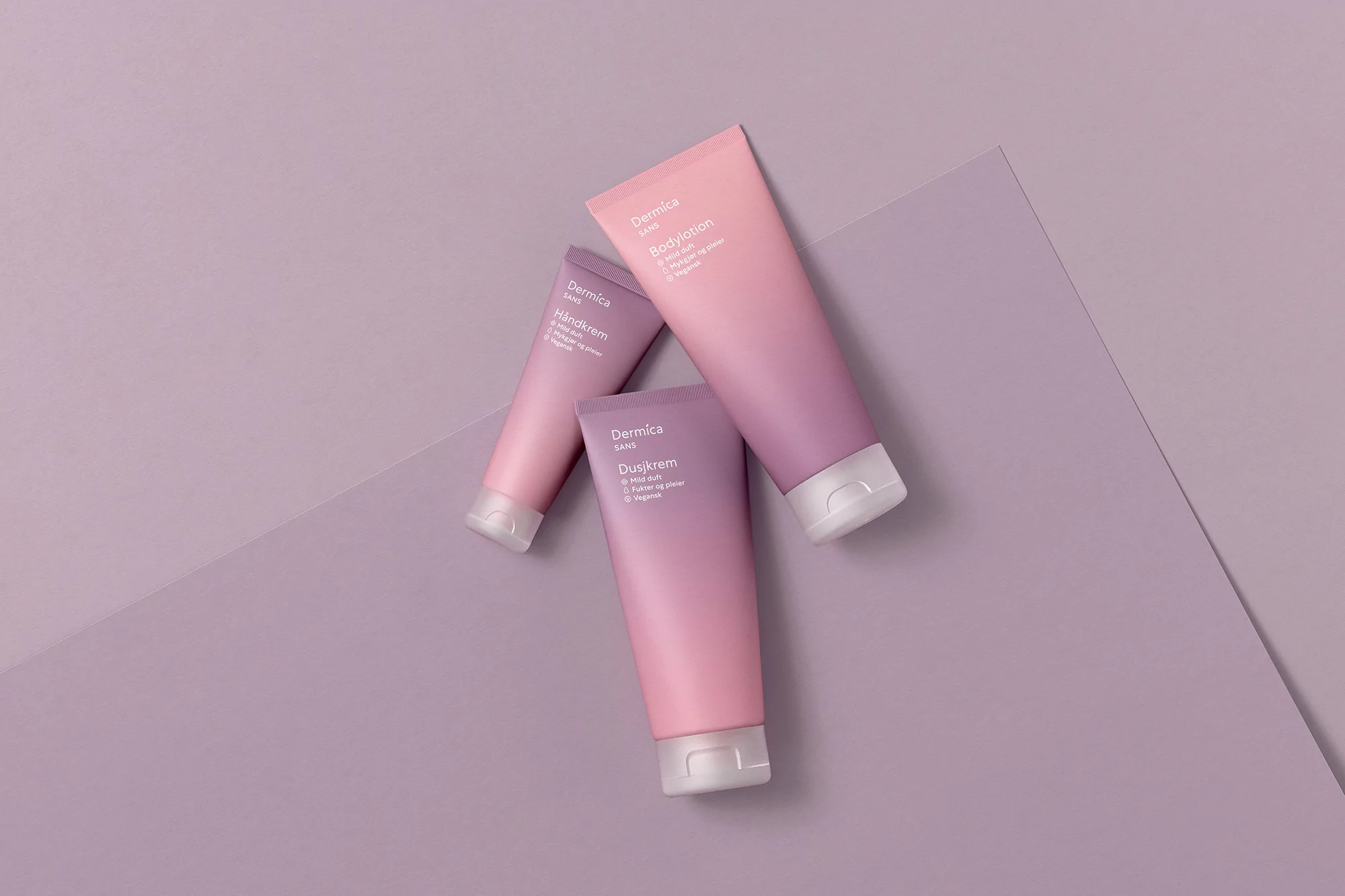 Three Dermica Sans body lotion and hand cream tubes in shades of pink and purple are displayed on a light purple surface.