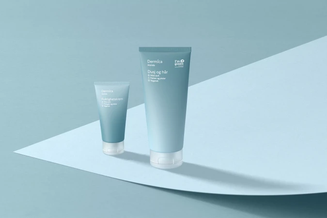 Two light blue Dermica MANN skincare tubes, one large and one small, sit on a light blue surface with a folded backdrop.