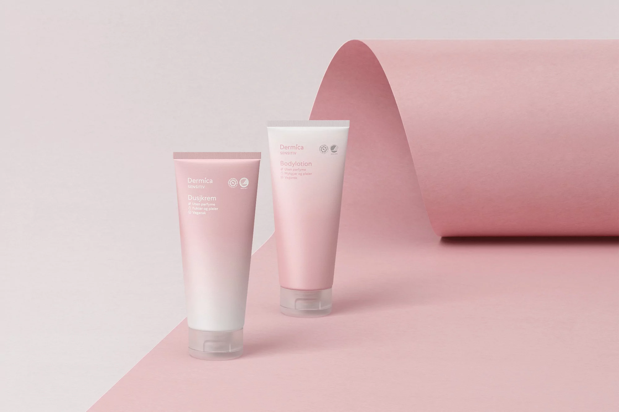 Two Dermica skincare tubes of body lotion and cream on pink backdrop. Minimalist beauty product shot for cosmetics brand promotion.