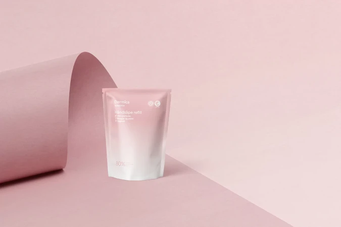 Dermica skincare refill pouch on a pink surface with a curved pink backdrop for beauty and wellness product promotion.