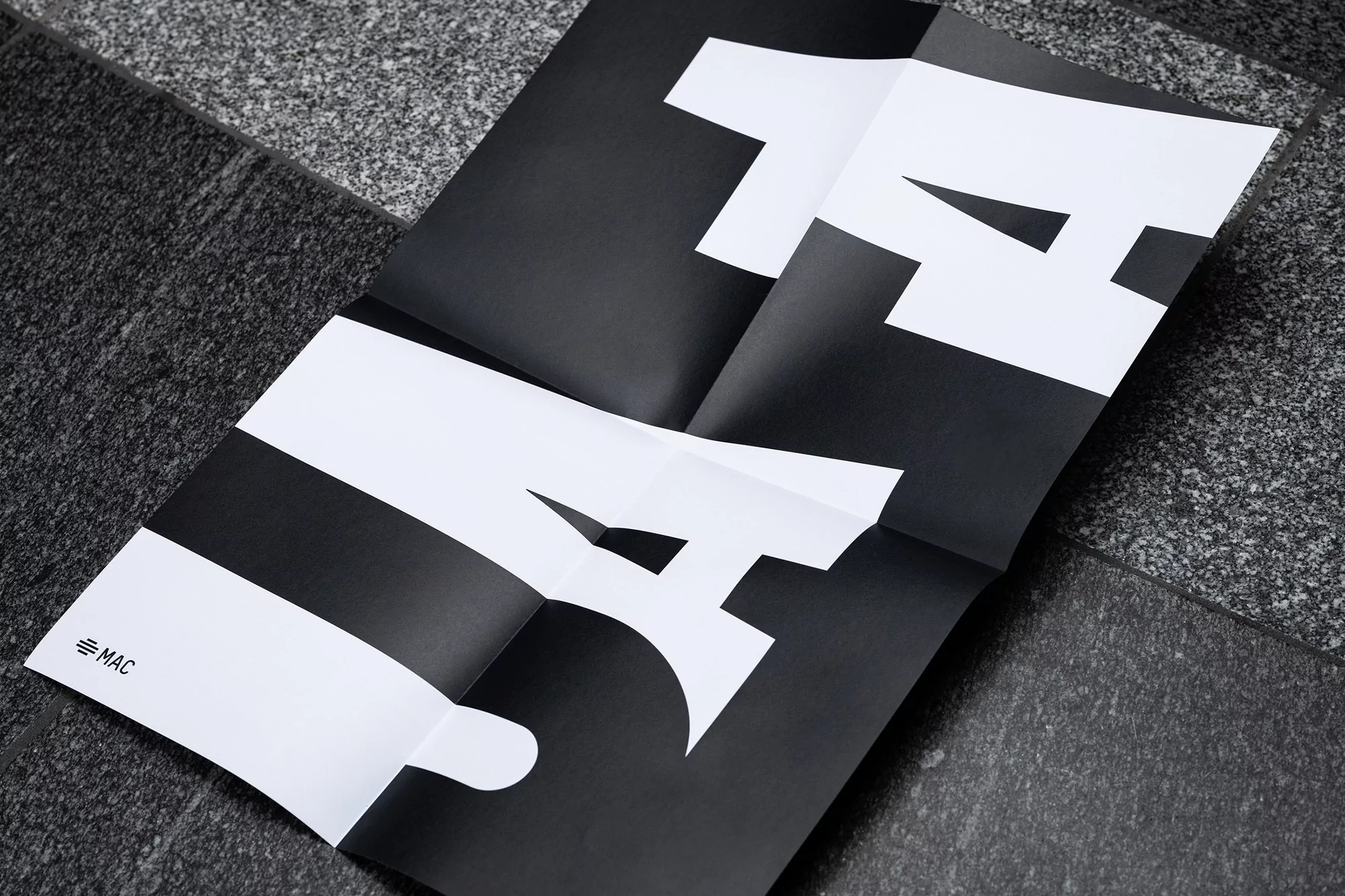 Folded black-and-white poster on a gray stone surface shows the cropped, stylized letters 'LA' for Los Angeles.