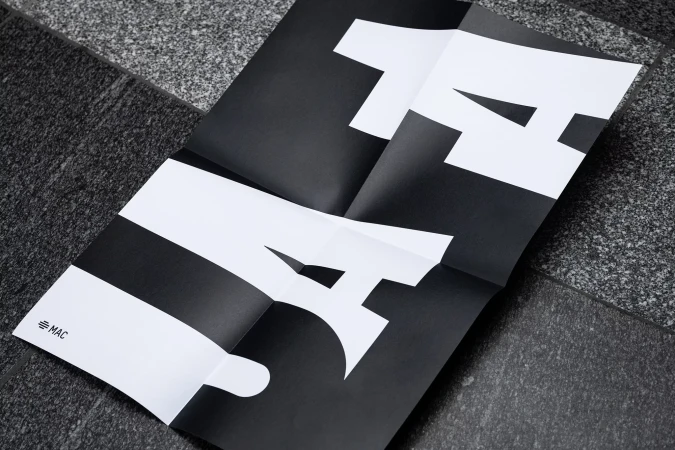 Folded black-and-white poster on a gray stone surface shows the cropped, stylized letters 'LA' for Los Angeles.
