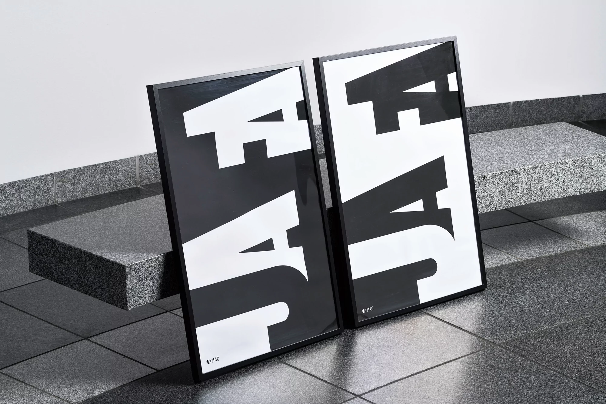 Two framed black-and-white typographic posters lean against a grey granite bench and tiled floor in an indoor environment with neutral lighting.