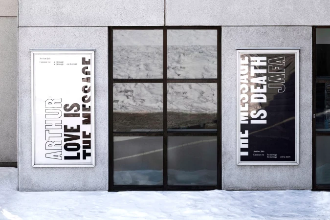 Exterior shot of two framed posters by Arthur Jafa on the exterior wall of a building next to a window in a snowy environment.