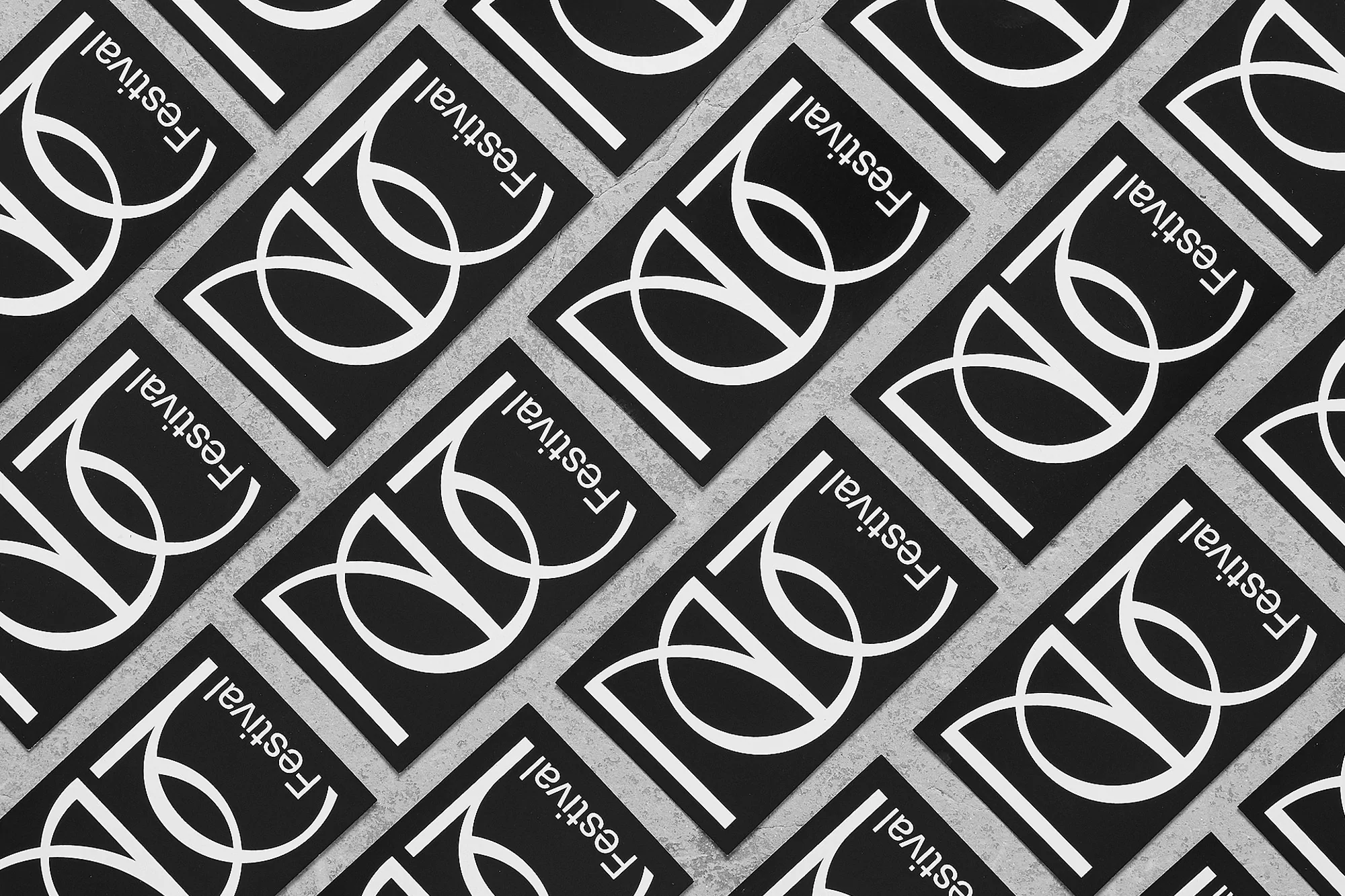 Pattern of black and white event posters featuring stylized logo and the word 'Festival' laid out on a textured gray surface.