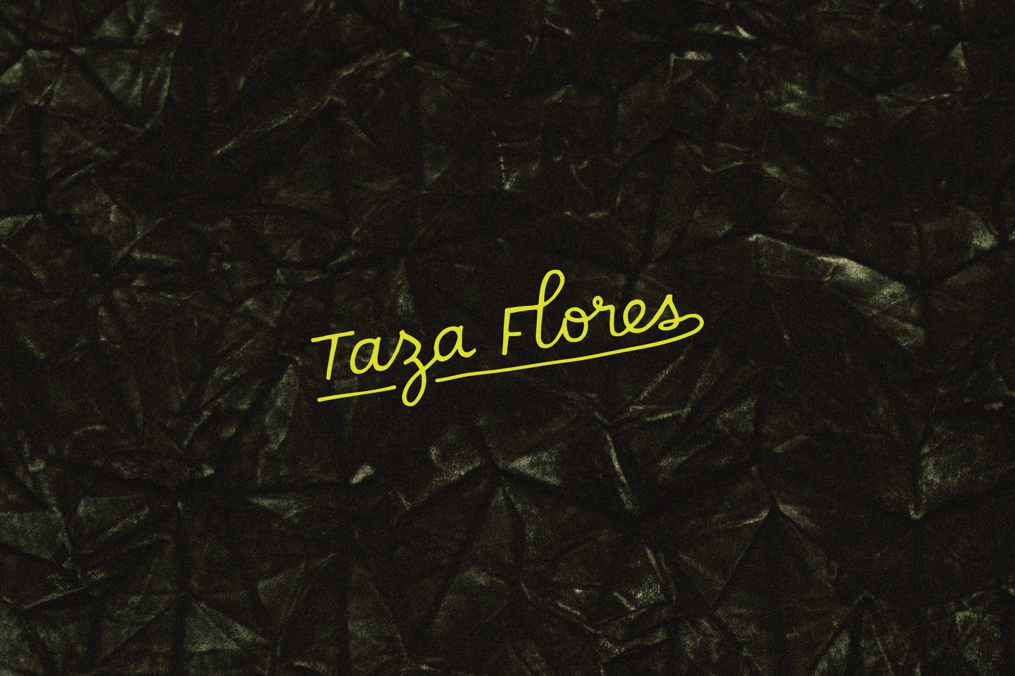 Dark crumpled textile backdrop with golden handwritten 'Taza Flores' branding across the center, creating a moody and artistic composition.
