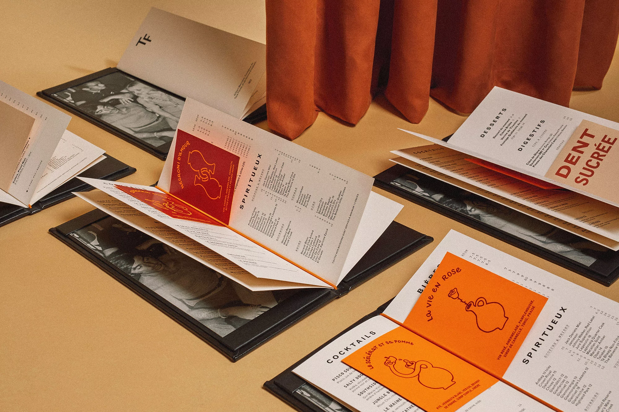 Several open restaurant menus are displayed on a tan surface with a rust-colored drapery in the background, showcasing the menu designs.