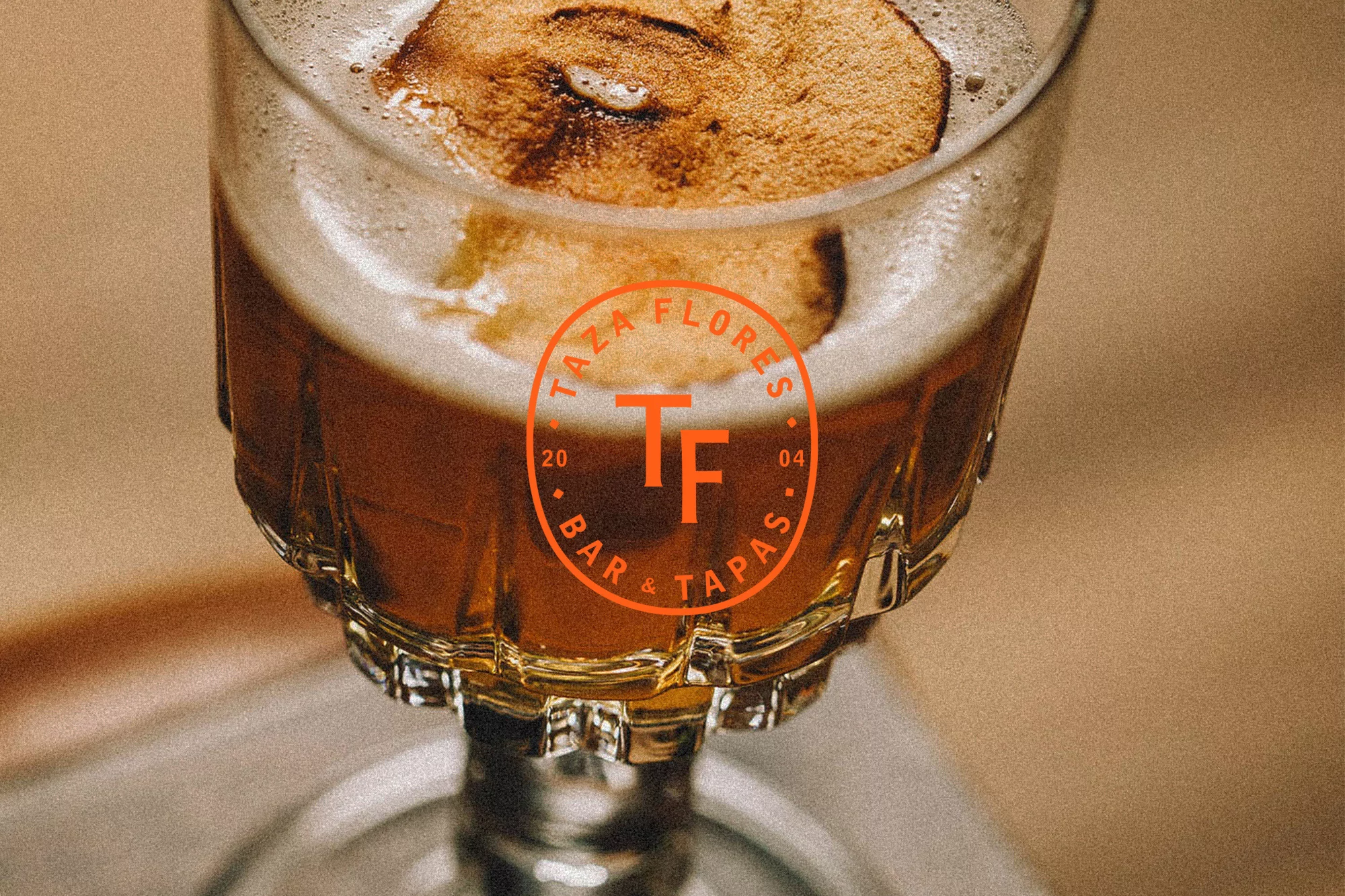 Close-up of a stemmed glass filled with amber liquid, topped with a foamy head and garnished with a round slice of dehydrated fruit.