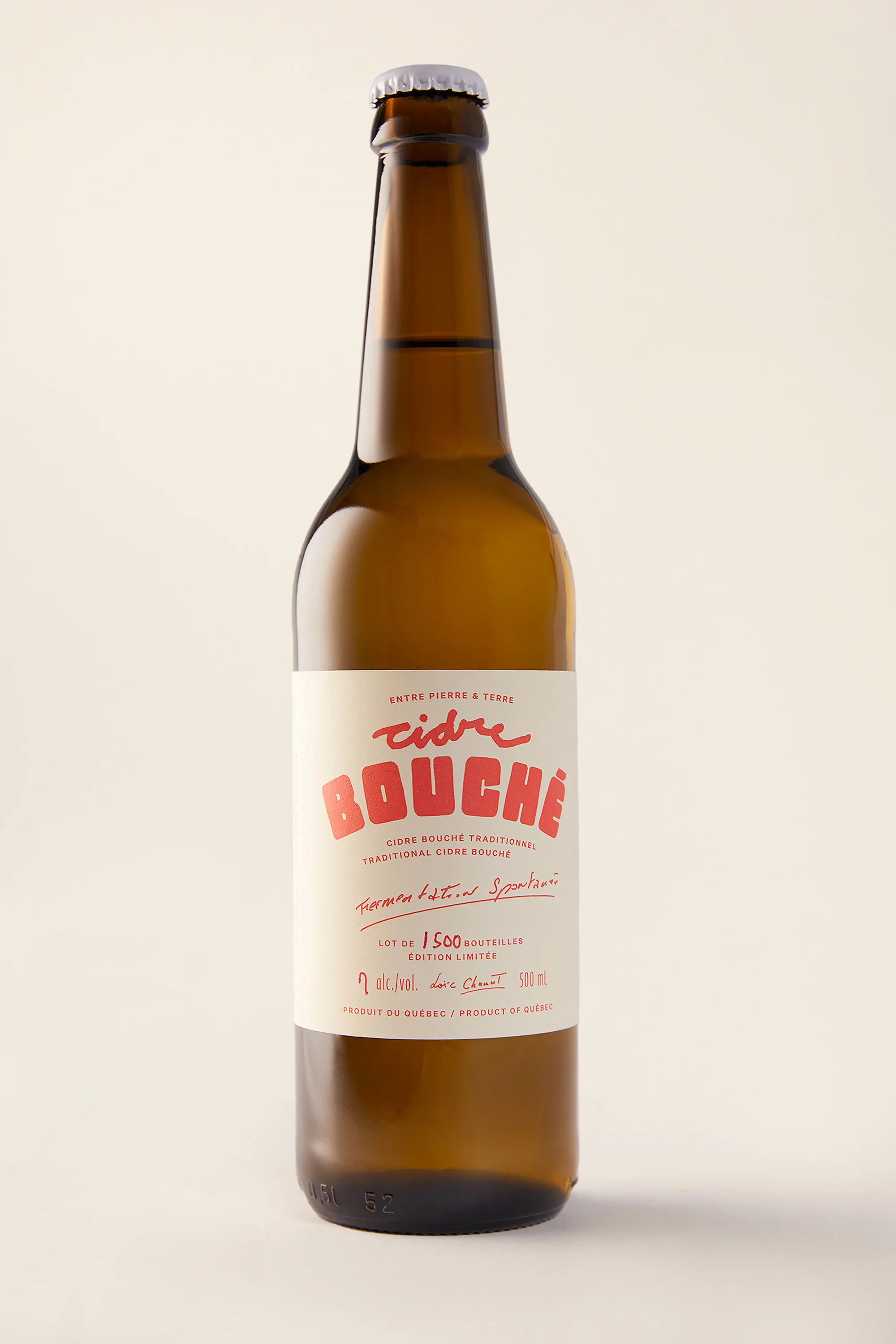 Studio shot of a brown glass cider bottle featuring a white label with red text against a neutral backdrop. Food and beverage.
