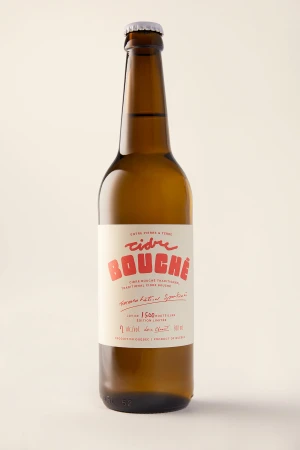 Amber glass bottle of cider with a cream label and red typography standing against a pale background