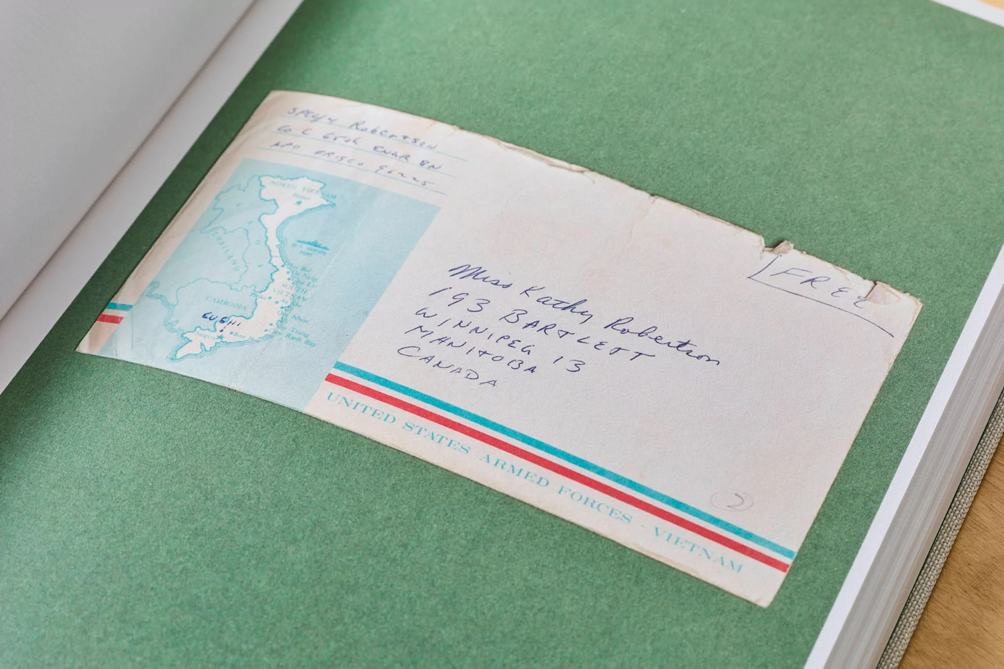 Vintage airmail envelope with a map of Vietnam, featuring handwritten addresses and postage, placed on a green page of a book.