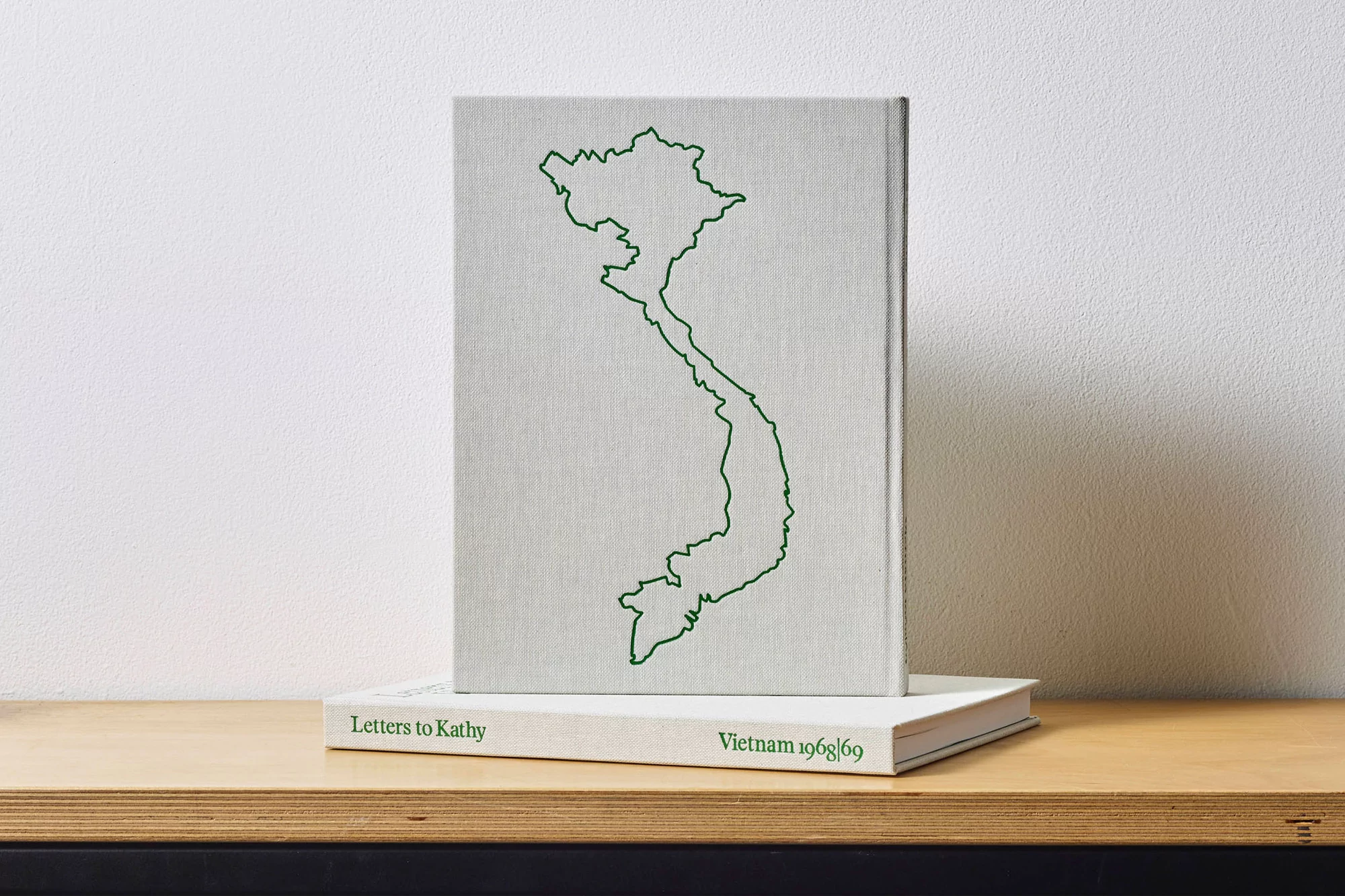 Book cover with a green outline of Vietnam, sitting atop another book on a light wood surface against a white wall backdrop.