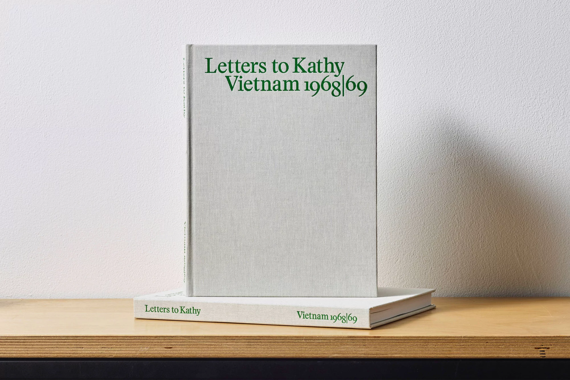 Two hardcover books stacked on a wooden surface against a white wall. The top book's title is 'Letters to Kathy Vietnam 1968|69'.