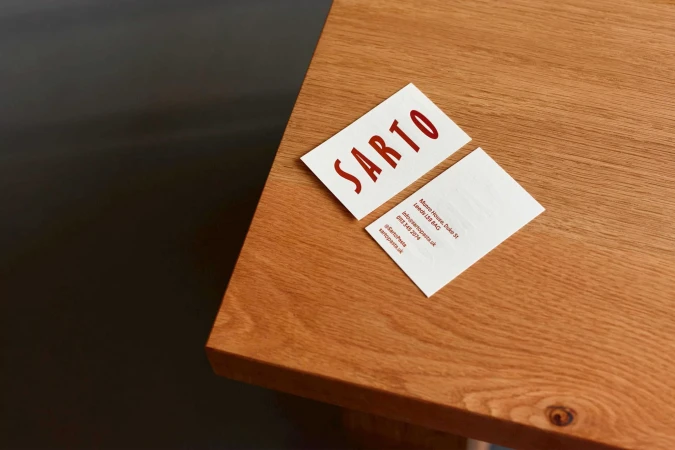 Two business cards with the word 'SARTO' on a wooden surface with a dark background in soft, diffused light.