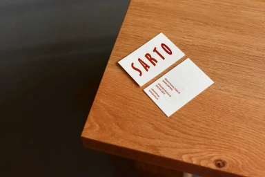 Two white business cards with red typography placed on a wooden table surface viewed from an elevated angle.