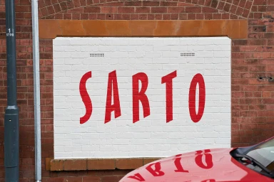 Red painted SARTO brand typography on a white brick panel framed by red brickwork exterior