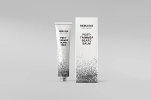 REMAINS post-trimmer beard balm tube and matching white box packaging against a grey studio backdrop