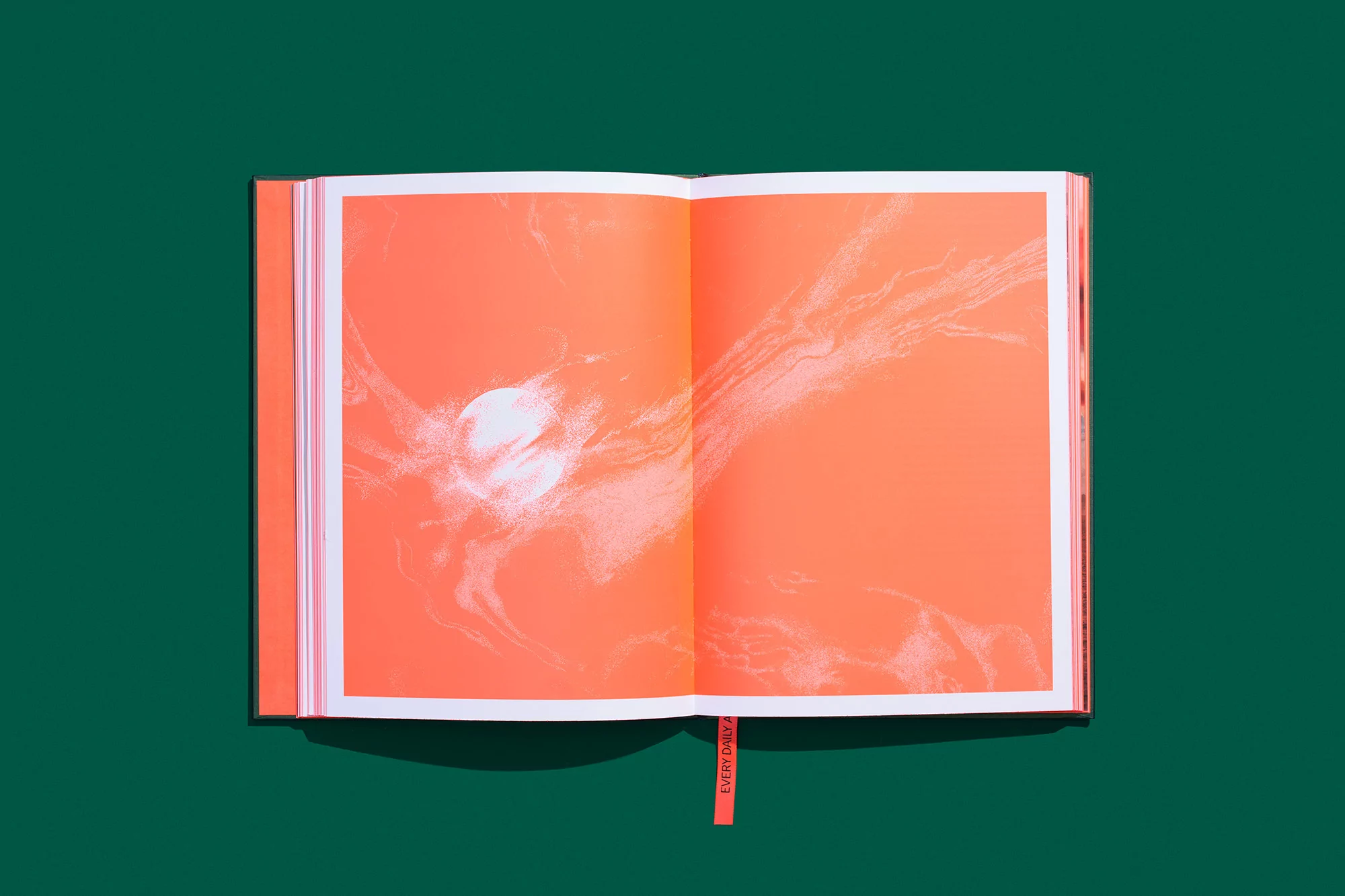 Open book with abstract orange and white design on pages, set against a dark green background in a studio setting.