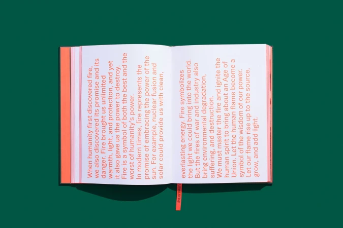 Close-up studio shot of an open book with text about fire, set against a solid green background with an attached orange bookmark.