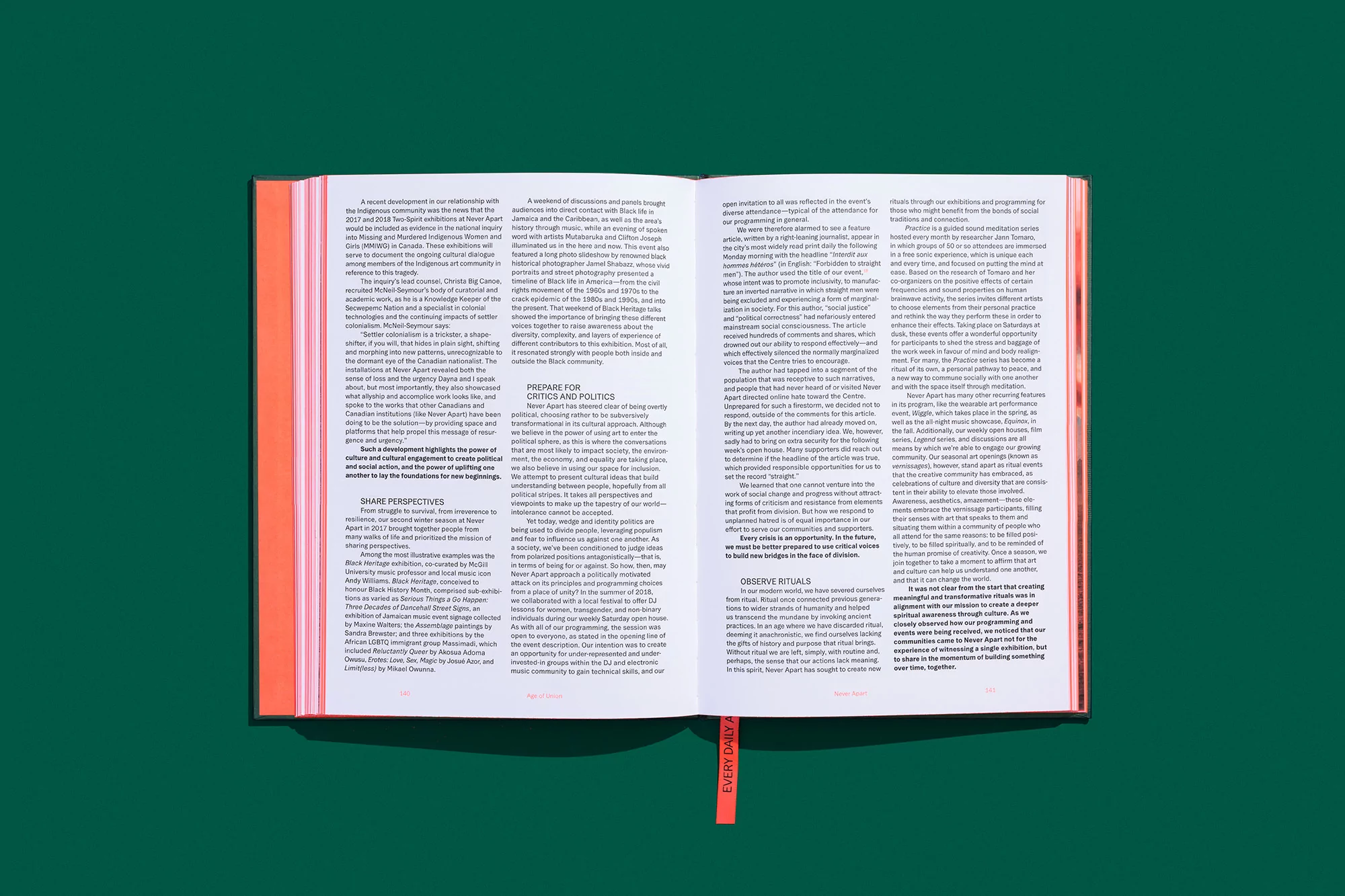 Open book with vivid coral cover and green backdrop, displaying text across two pages, top-down view, showcasing editorial content.