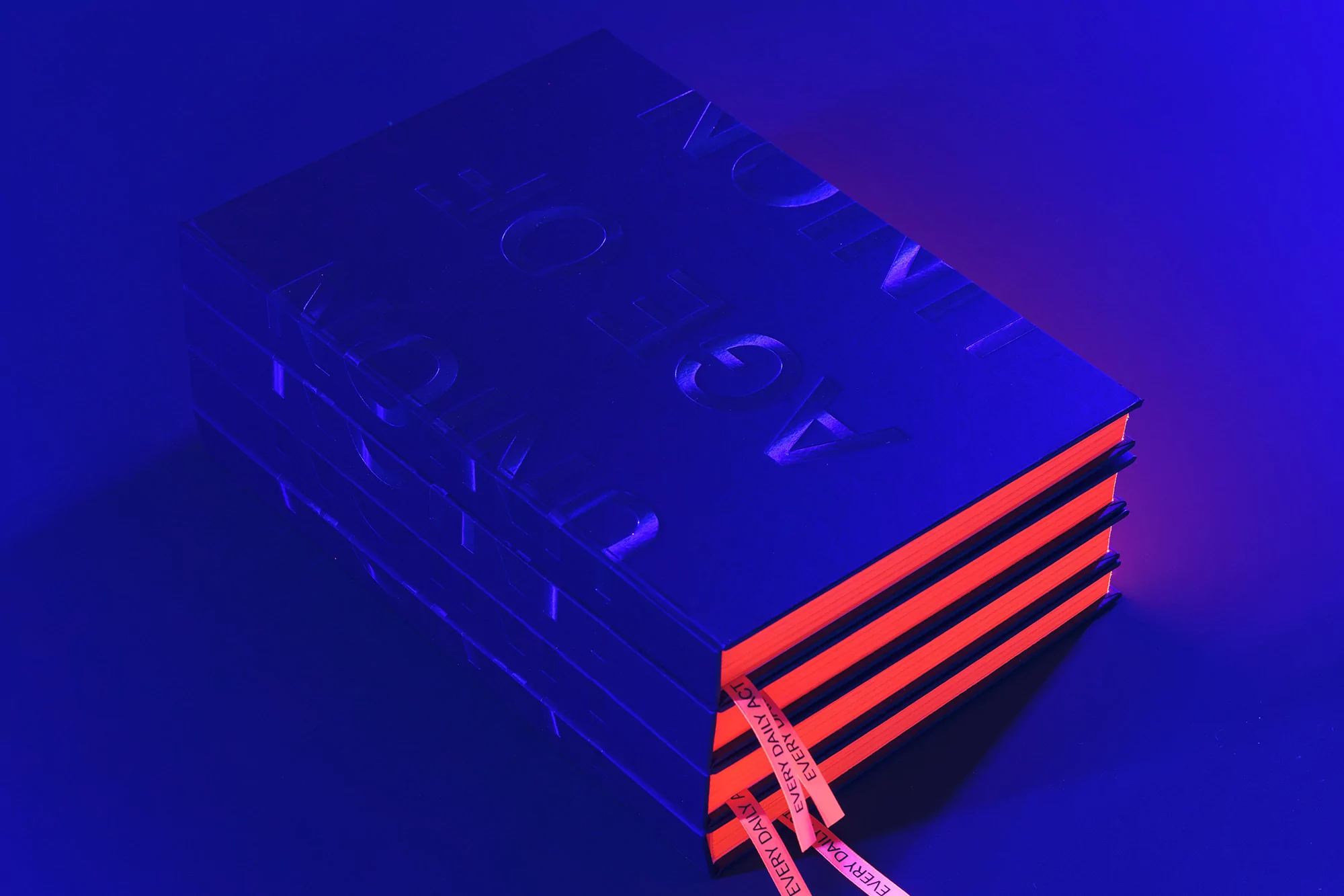 Dark blue hardcover book with orange edges and ribbon bookmark lying on a dark blue surface, low-key lighting. 