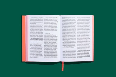 Open book with multiple columns of text displayed flat on a dark green solid background with an orange ribbon bookmark.