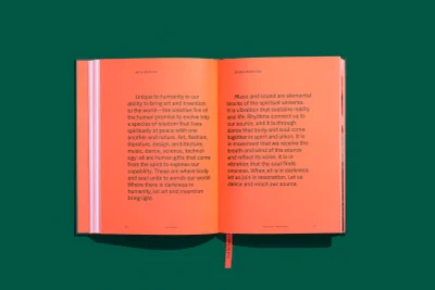 Open orange book with black typographic text laid flat against a solid green background surface.