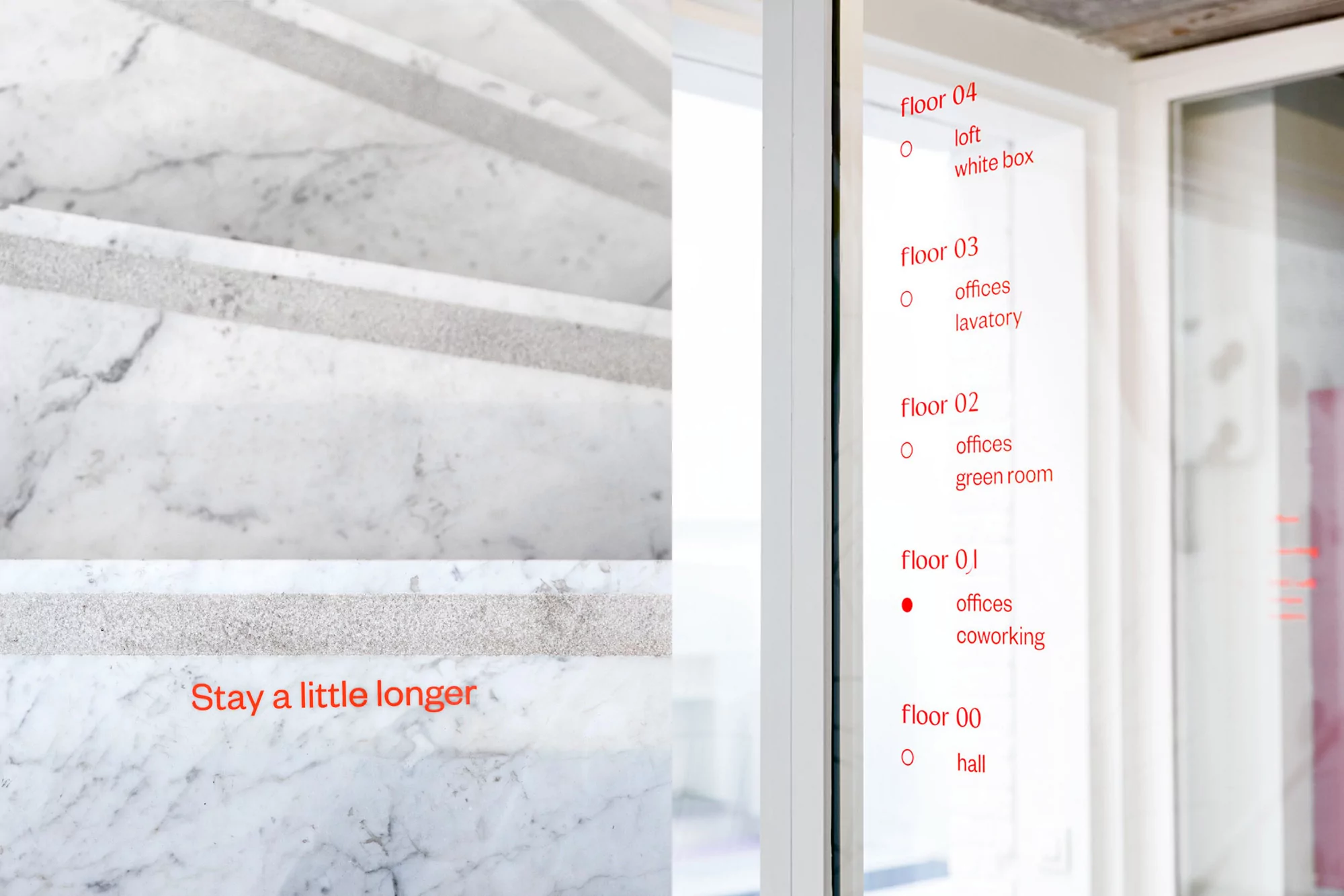 Minimalist interior with marble stairs and red text signage for building floors: loft, office, hall, and coworking spaces.