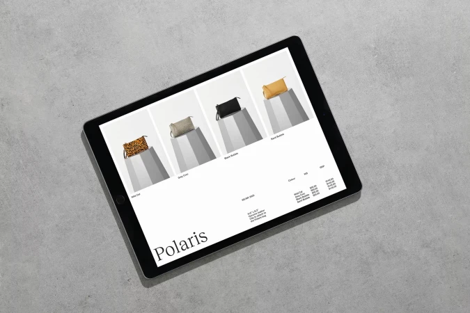 A digital tablet displaying an e-commerce website product page for leather handbags resting on a grey concrete surface