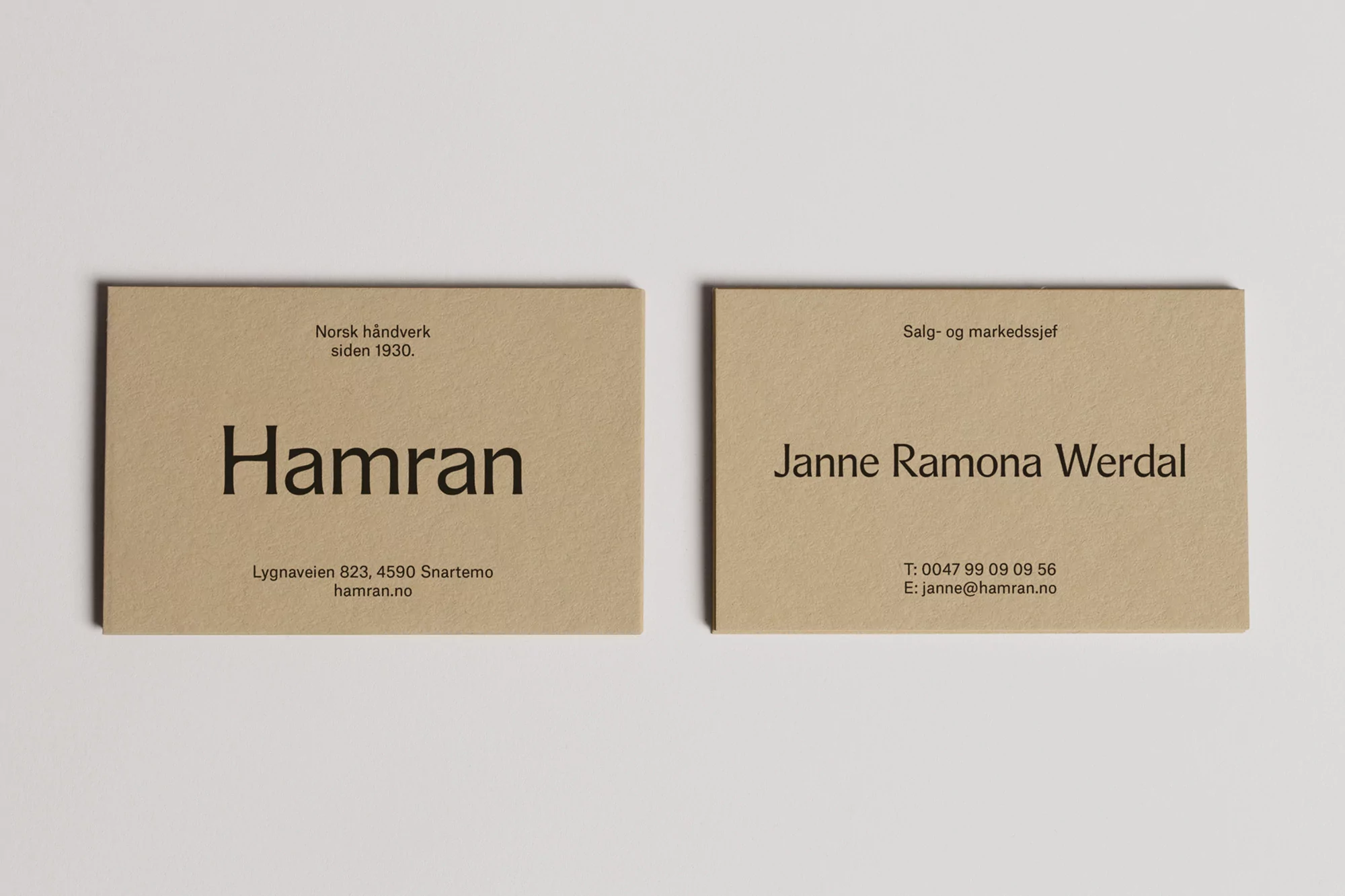 Two minimalist business cards on a white surface feature company and contact information in a sans-serif typeface against a tan backdrop.