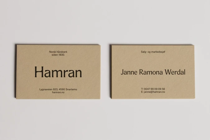 Two minimalist business cards on a white surface feature company and contact information in a sans-serif typeface against a tan backdrop.