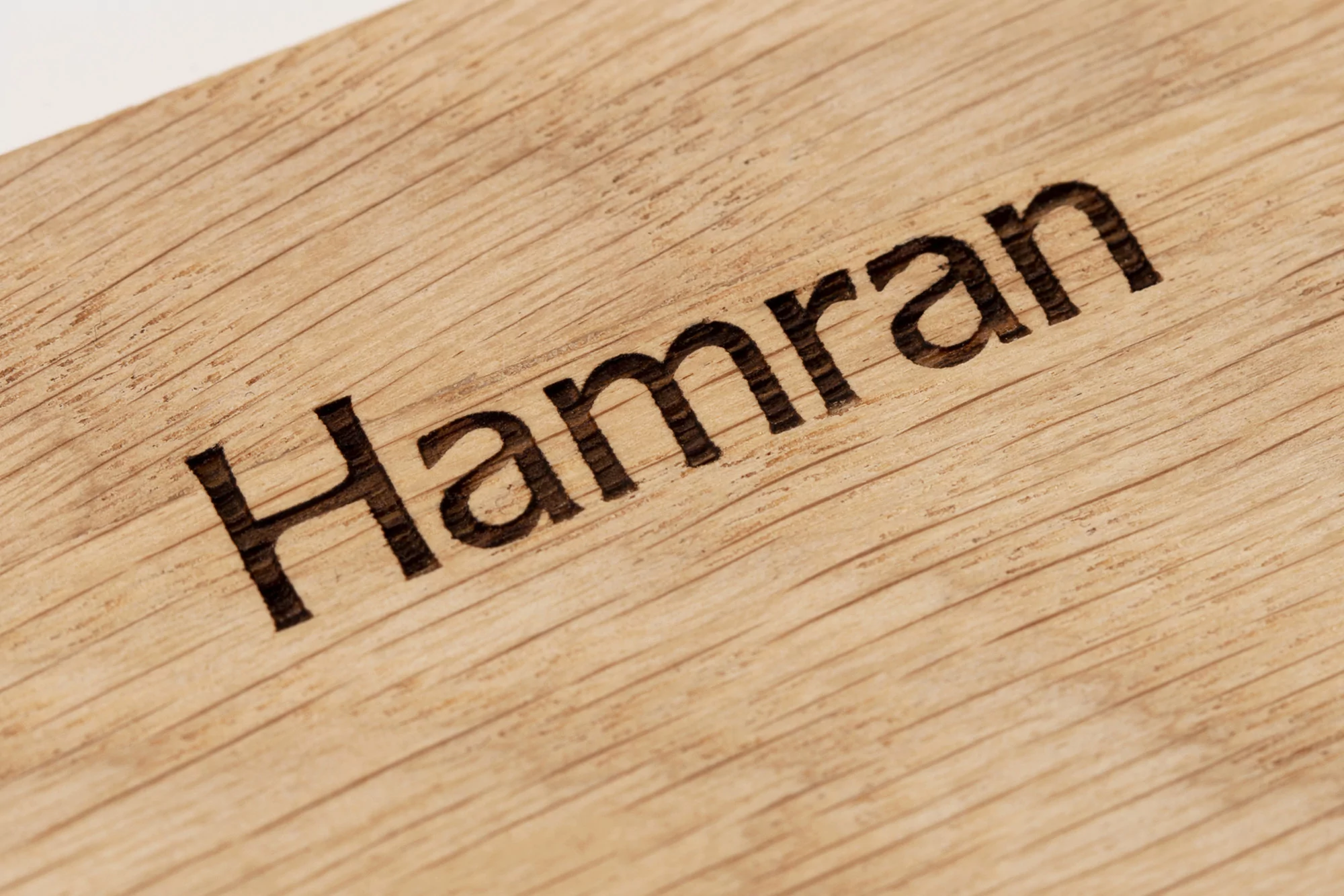 Close-up of a light brown wooden surface with the name 'Hamran' deeply engraved, showcasing its woodgrain detail and craftsmanship.