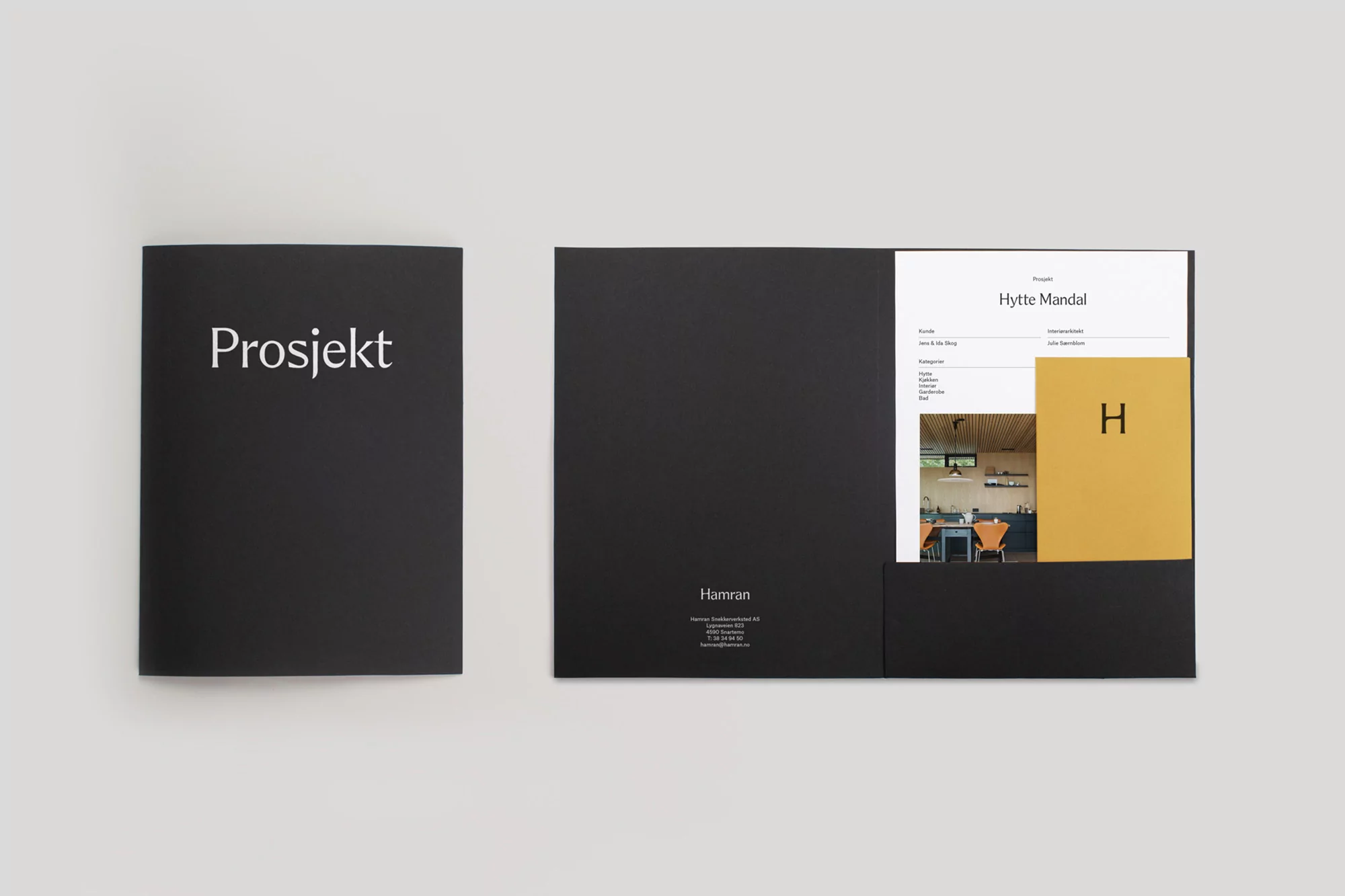 Two black folders with white text sit on a white surface, one open to reveal interior design images and brand elements.