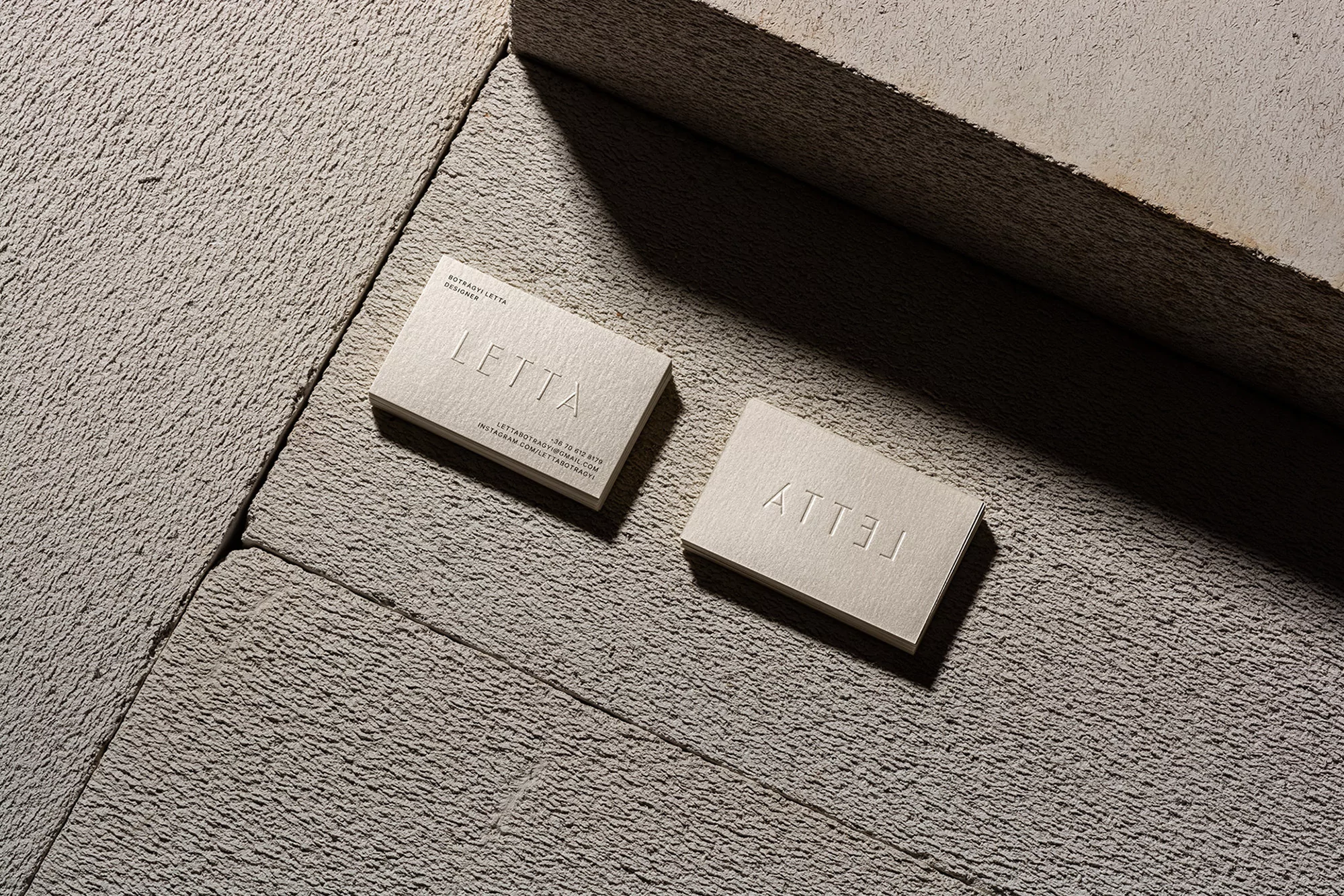 Close-up of two business cards with embossed text, arranged on a textured concrete surface in a studio setting with controlled lighting.