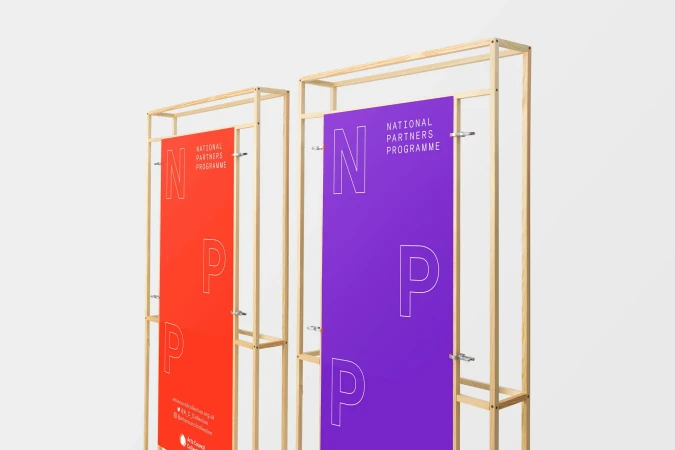 Two promotional banners with metal stands display white text on red and purple, creating a modern graphic presentation against a neutral backdrop.