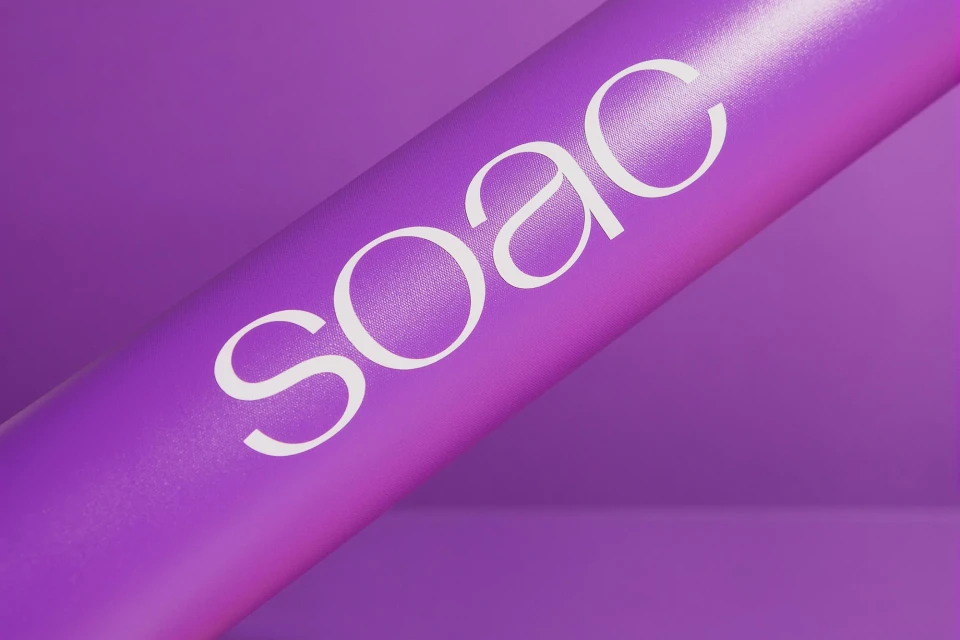 Purple background with a cylindrical object displaying 'SOAC' in white font, creating a modern and minimalist visual.