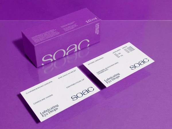 Close-up of a skincare product box and business cards on a purple surface showcasing branding, packaging, and product details.