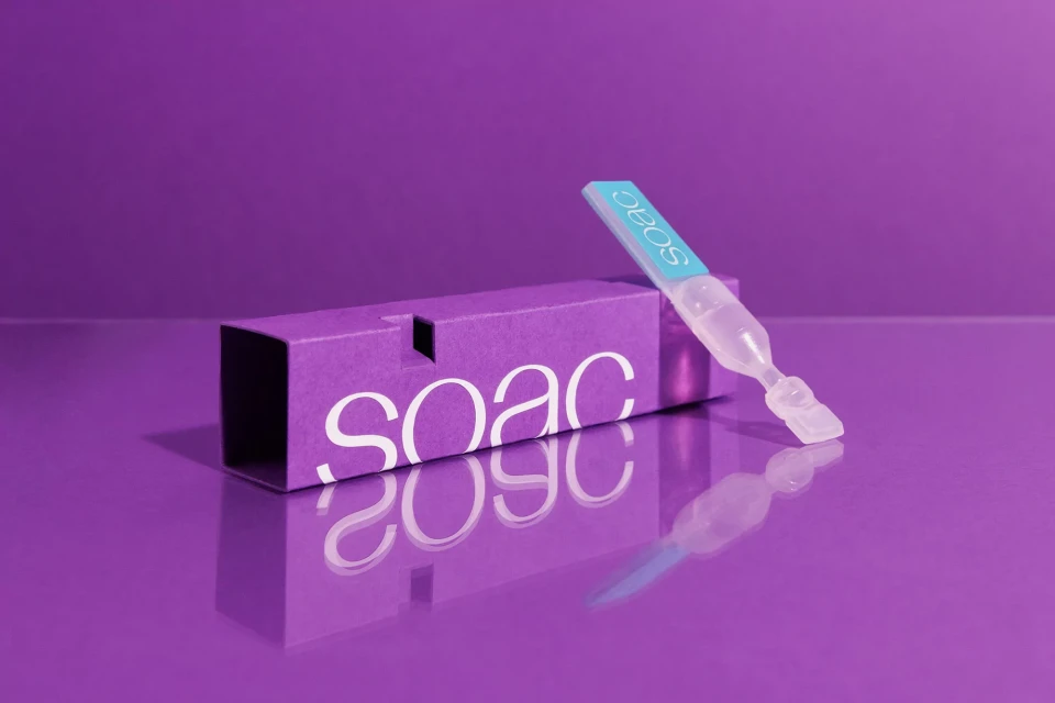 Product shot of a clear vial and a purple box with the word 'SOAC' on both, set against a matching purple background.