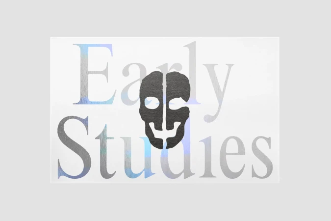 Graphic design with a stylized black skull centered on a white background, overlaid with translucent iridescent text reading 'Early Studies'.