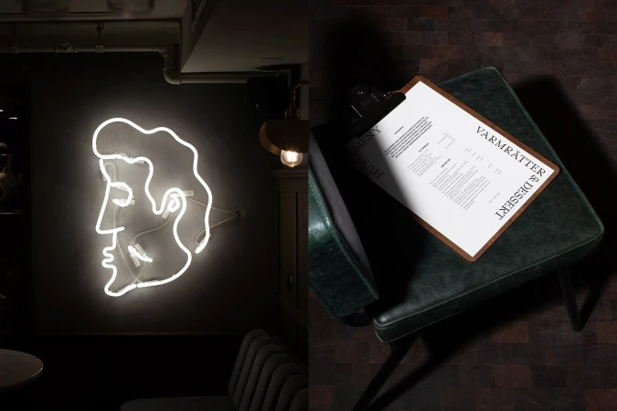 Neon art of a face on a wall, beside a dark green seat with a menu leaning on it in a moody, contrasted interior space.