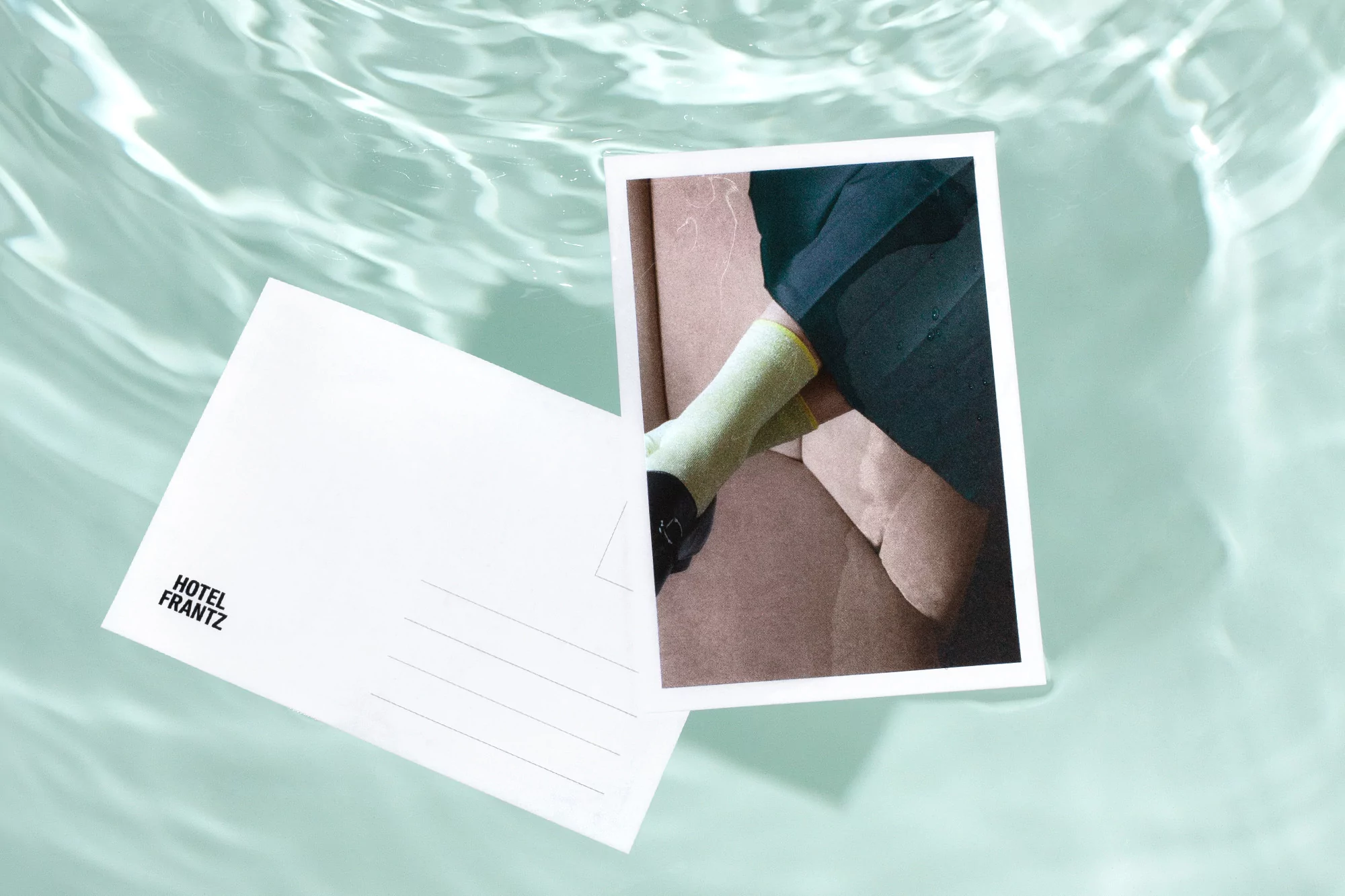 Postcard floating in water features a photograph of a person in dark clothing with yellow-green socks, next to brand postcard.