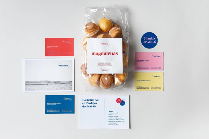 Overhead shot of Ordeniz brand Magdalenas in a plastic bag surrounded by business cards and stationery on a white surface.