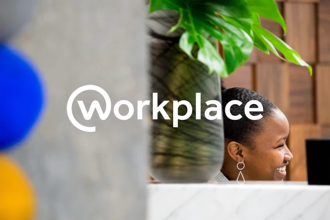Business image featuring an adult woman smiling in an office setting with a plant, marble counter, and the 'Workplace' logo.