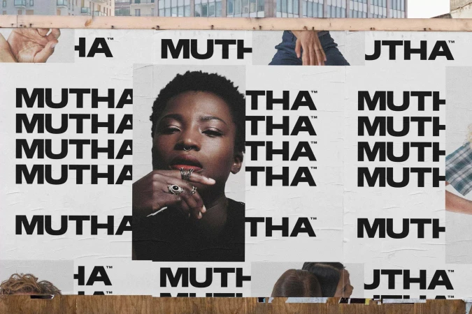 Portrait of an African-American woman with jewelry displayed on a billboard covered with a black-and-white text pattern, set in an urban area.