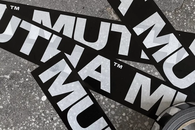 Black and white MUTHA brand stickers overlapping on a textured concrete surface.