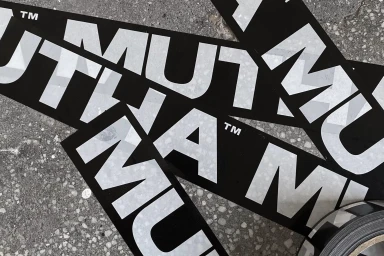 Black and white MUTHA brand stickers overlapping on a textured concrete surface.