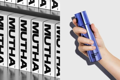 Hand holding a metallic blue MUTHA body oil bottle against a clean white background next to branded product boxes