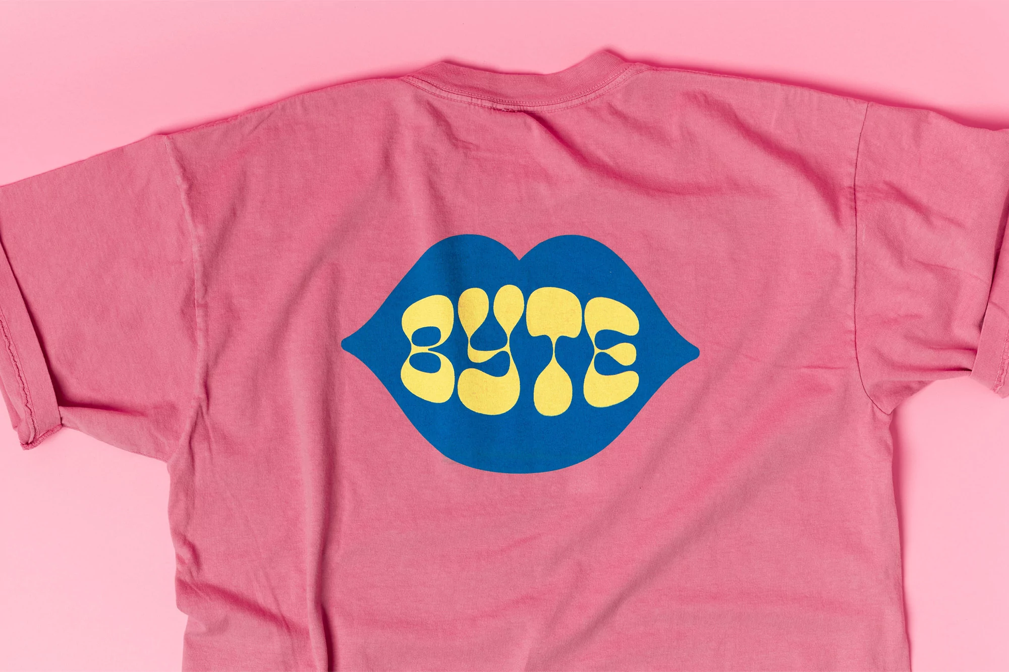 Pink t-shirt with a graphic of blue lips and the yellow text "BYTE" in a stylized font against a solid pink background.