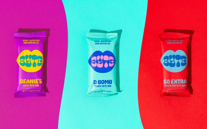 Eye-level shot of three brightly colored Byte brand snack bars: purple, turquoise, and red, evenly spaced against their corresponding backgrounds.